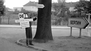Der DEFA-Wegweiser zeigt das Schild "Auskunft" und ist dreisprachig.