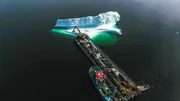 Ein Eisberg wird "geerntet". Der Bagger tr&auml;gt gro&szlig;e Brocken ab. Das reine Eisbergwasser ist begehrt f&uuml;r die Herstellung von Cidre, Bier und Wodka.