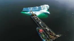 Ein Eisberg wird "geerntet". Der Bagger tr&auml;gt gro&szlig;e Brocken ab. Das reine Eisbergwasser ist begehrt f&uuml;r dieHerstellung von Cidre, Bier und Wodka.