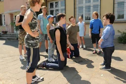 Vor dem Eingang des Kinderheims sucht der kleinw&uuml;chsige Tom (Jordan Prentice, r.) seinen vermeintlichen Sohn Michi (Luis Vorbach, 4.v.l.). F&uuml;r die Heimbewohner ein willkommener Anlass, Michi wegen seiner Angeberei &uuml;ber seinen gro&szlig;artigen Vater blo&szlig;zustellen.