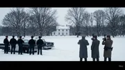 Eine Gruppe uniformierter Personen steht neben Polizeifahrzeugen auf einem schneebedeckten Gel&auml;nde, w&auml;hrend mehrere andere Personen ein wei&szlig;es Haus im Hintergrund fotografieren.