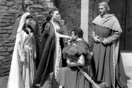 Sir Lancelot (Robert Taylor, 2.v.r.) k&uuml;sst K&ouml;nigin Guinevere (Ava Gardner, 3.v.l.) die Hand. Seine Frau Elaine (Maureen Swanson, li.), Percival (Gabriel Woolf, re.) und K&ouml;nig Artus (Mel Ferrer, 2.v.l.) wohnen der Szene bei.