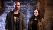 Hosts Nick Groff and Katrina Weidman stand in front of basement brick wall.