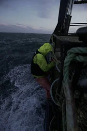 A crew member on the Brenna A hangs off the side of the stack to tie pots off.