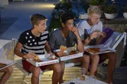 Robin (l.), Leroy (M.) und Luc (r.) entspannen mit Pizza am Pool.