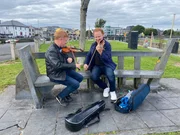 Sean Smyth und Daniel Hope musizieren auf einer Bank.