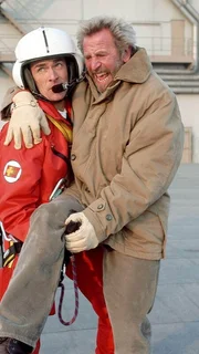 Sanit&auml;ter Ralf Staller (Wolfgang Krewe, li.) st&uuml;tzt den vor Schmerzen st&ouml;hnenden Gruber (Hermann Giefer), um ihn zum Medicopter und damit in Sicherheit zu bringen.