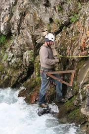 Dustin Hurt drills wall brackets into the steep wall of riverbank.