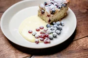 Auf dem Bild ist die Nachspeise auf einem Teller zu sehen. Es gibt Heidelbeer-Clafoutis mit Vanilleso&szlig;e.