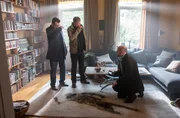 Die Kommissare Finn (Sven Martinek, l.) und Lars (Ingo Naujoks, 2.v.l.) stehen am Fundort der Leiche von Hans Vonnsen. Auf dem Teppich vor ihnen ist ein dunkler Abdruck des bereits stark verwesten K&ouml;rpers zu sehen. Dr. Henning Strahl (h. r.) kniet auf dem Boden und dokumentiert den Tatort mit seiner Kamera.