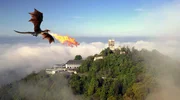 Ein feuerspeiender Drache (KI-generiert) &uuml;ber dem Drachenfels, der sich im Morgennebel &uuml;ber dem Rheintal erhebt. Der Mythos vom Fabelwesen regt bis heute die Fantasie der Besucher an und macht einen Gro&szlig;teil der Anziehungskraft des Berges aus.