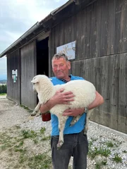 Der Bauer h&auml;lt vor dem Stall das junge Lamm im Arm.