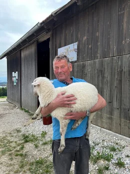 Der Bauer h&auml;lt vor dem Stall das junge Lamm im Arm.