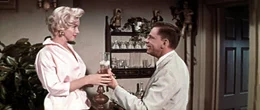 Kaum ist seine Frau aus dem Haus, "tanzen bei Richard (Tom Ewell, r.) die M&auml;use auf dem Tisch". Der Strohwitwer verliebt sich Hals &uuml;ber Kopf in seine junge Nachbarin (Marilyn Monroe, l.) ...