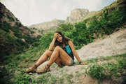Eva sits on the edge of a rock with handmade running sandals on.
