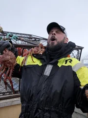 Mittlere Einstellung von Birgerson-Deckhelfer Ronnie, der eine Krabbe h&auml;lt und feiert.