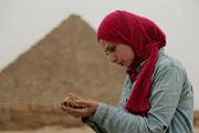 Kairo, Ägypten - Sara steht vor den Pyramiden und betrachtet ein Knochenfragment, das in einem der Gräber gefunden wurde. (Windfall Films) Kairo, Ägypten - Sara steht vor den Pyramiden und betrachtet ein Knochenfragment, das in einem der Gräber gefunden wurde. (Windfall Films)