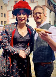 Auf dem Freiburger M&uuml;nstermarkt ist S&ouml;ren Anders (re.) mit Dragqueen und Stadtf&uuml;hrerin Betty BBQ unterwegs und probiert die legend&auml;re "Lange Rote im Weckle".