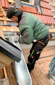 Der Spengler montiert die Dachrinne. Bald kann die Rinne ihren Job machen und den Regen vom Dach ableiten.