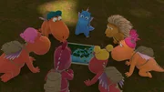 Auf dem Waldboden kniend, sind der kleine Drache Drache Kokosnuss und seine Freunde konzentriert &uuml;ber eine Landkarte gebeugt.