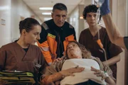 Greta (Lydia Amasko, r.) und Elke (Marie Rosa Tietjen, l.) starten in ihre gemeinsame Schicht. Doch schnell zeigt sich: Heute wird es herausfordernd. Direkt zu Beginn wird die schwangere Vicky (Thea Rasche, 2.v.r.) eingeliefert, die nach einem Verkehrsunfall schnellstens untersucht werden muss.