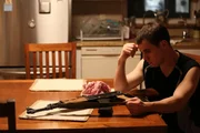 Derek with gun at table, hand on head. Derek with gun at table, hand on head.