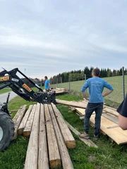 Der alte- und junge Landwirt helfen einander beim Stapeln von Holzbrettern.