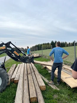 Der alte- und junge Landwirt helfen einander beim Stapeln von Holzbrettern.