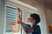Eik (Xavier Ziegler Ribeiro) h&auml;ngt einen orangenen Papierdrachen an die Gardinenstange. So m&ouml;chte er an seine k&uuml;rzlich verstorbene Mutter erinnern.