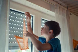 Eik (Xavier Ziegler Ribeiro) h&auml;ngt einen orangenen Papierdrachen an die Gardinenstange. So m&ouml;chte er an seine k&uuml;rzlich verstorbene Mutter erinnern.