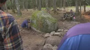 Eine Gruppe von Menschen untersucht den Boden um einen Stein.