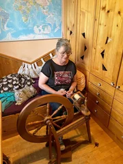 Die B&auml;uerin stellt mit der Handspindel aus ihrer eigenen Schafswolle das neue Garn her. Neben ihr sitz eine Katze.