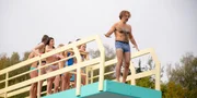 Immer wieder nimmt Dr. Rieger (Rick Kavanian) Anlauf, um vom Brett zu springen, schafft es dann aber doch nicht, und h&auml;lt den ganzen Laden auf.