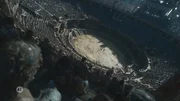 Ein riesiges antikes Amphitheater ist mit Zuschauern gef&uuml;llt, w&auml;hrend in der Mitte auf der sandigen Arena ein Kampf stattfindet.