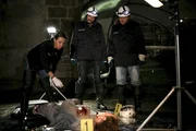 Die Gerichtsmedizinerin Dr. Julia Trautmannsdorff (Sandra Cervik, l.) weist ihre Kollegen Major Carl Ribarski (Stefan J&uuml;rgens, M.) und Oberstleutnant Helmuth Nowak (Gregor Seberg, r.) auf etwas Ungew&ouml;hnliches an dem Opfer hin.