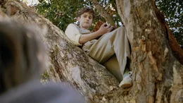 Der homosexuelle Schriftsteller Owen James (Fionn O'Shea) liest auf einem Baum aus seinem Gedichtband vor.