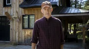 Ein Mann steht vor einem Holzhaus, das mit einem dekorativen Elchgeweih verziert ist.