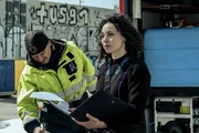 Polizeitaucherin Kiki (Marie Vinck) fragt sich, zu wem die gefundene Hand geh&ouml;rt. Neben ihr steht ein Arbeiter in Warnschutzjacke (Schauspieler unbekannt).