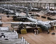 Eine große Industriehalle zeigt Reihen von Bombern in verschiedenen Montagephasen, während Arbeiter um sie herum tätig sind. Eine große Industriehalle zeigt Reihen von Bombern in verschiedenen Montagephasen, während Arbeiter um sie herum tätig sind.