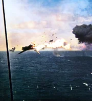 Ein brennendes Flugzeug stürzt über dem Meer ab, während Explosionen und Rauch die Wasseroberfläche in einem heftigen Gefecht einhüllen. Ein brennendes Flugzeug stürzt über dem Meer ab, während Explosionen und Rauch die Wasseroberfläche in einem heftigen Gefecht einhüllen.