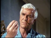 R. R. Benson (Leslie Nielsen) betrachtet die Kugel, an der er hätte sterben können, die aber von seiner Bibel abgefangen wurde. R. R. Benson (Leslie Nielsen) betrachtet die Kugel, an der er hätte sterben können, die aber von seiner Bibel abgefangen wurde.