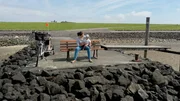 NDR Fernsehen DIE NORDSTORY - FAMILIENSTRESS AUF HALLIG S&Uuml;DEROOG. Nele Wree mit ihrer j&uuml;ngsten Tochter auf einer Bank auf Pellworm, von der man Richtung S&uuml;deroog blicken kann.