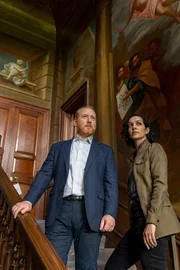 Max (Adrian Scarborough) und Priya (Sonita Henry) auf der verzierten Treppe der internationalen Schule von Chelsea.