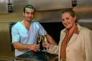 Benedikt F&ouml;rster (Florian W&uuml;nsche) und Prof. Dr. Lisa Wolter (Eva Maria Bayerwaltes) sto&szlig;en auf Benedikts erfolgreiches Erlangen des Doktortitels an.