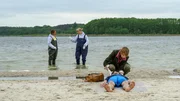 In Wismar h&auml;lt sich seit Jahrzehnten ein hartn&auml;ckiges Ger&uuml;cht. Im Neuklostersee soll sich ein Riesenwels befinden, der auch Menschen und Tiere angreift. F&uuml;r Dr. Helene Sturbeck (Katharina Blaschke, r.) und Kriminaltechnikerin Roswitha Prinzler (Silke Matthias, M.) ist es allerdings fast ausgeschlossen, dass ein Fisch Jonas Gehrmann (Rasmus Max Wirth, liegend) h&auml;tte ertr&auml;nken k&ouml;nnen. Fast...