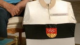 25 Jahre nach den Atombombenabw&uuml;rfen in Japan finden 1964 die Olympischen Sommerspiele in Tokio statt. Mitten im Kalten Krieg sollen die Spiele zu einem Symbol f&uuml;r eine friedliche Welt werden. Insbesondere das geteilte Deutschland soll dies unter Beweis stellen: Auf Anordnung des IOC m&uuml;ssen beide deutsche Staaten trotz tiefer ideologischer Gr&auml;ben mit einer gemeinsamen Mannschaft in Tokio antreten - Olympiatrikot Lothar Claesges.