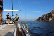 Santorini, Greece - Prof Evi Nomikou watches the cliffs of Santorini's southern tip from the bow of the boat as cameraman Will Fewkes and sound recordist Doug Dreger film GVs.  (MSP/Imogen Walford)