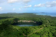 Der kreisrunde Kratersee von Lalolalo liegt tief im vulkanischen Krater mit steilen Felsw&auml;nden.