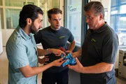 Adil (Omar Akbar, l.) erkl&auml;rt J&uuml;rgen Franke (Bruno F. Apitz, r.) sehr zum Missfallen von Bastian Schmid (Samuel Hummel, M.), dass dessen Spielzeugroboter nicht kindersicher ist und bietet sich an, das zu &auml;ndern.