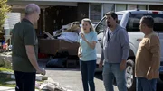 Mehrere Personen stehen vor einem Haus und diskutieren neben einem geparkten Pickup und einem Haufen Abfall.